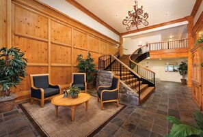 A spacious lobby with a wooden paneled wall, a stone staircase, and a chandelier. - Grand Lake | Couples Lake Retreat | Pool + Hot Tub (Afton)