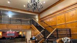 Un hall d’hôtel avec un grand escalier, des boiseries, un comptoir d’accueil et un lustre.
