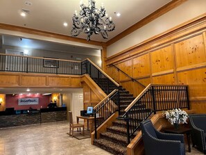A hotel lobby with a grand staircase, wooden paneling, a reception desk, and a chandelier. - Grand Lake | Couples Lake Retreat | Pool + Hot Tub (Afton)