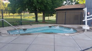 A swimming pool with a metal ladder, a hot tub, and a fenced area with trees in the background. - Grand Lake | Couples Lake Retreat | Pool + Hot Tub (Afton)