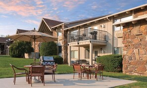 A patio with outdoor furniture, a grill, and a stone building with a balcony.