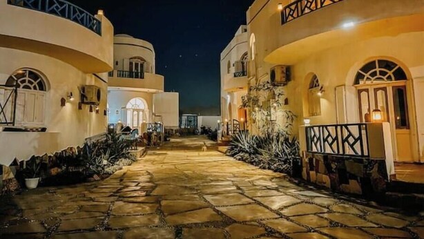 A stone-paved courtyard with buildings featuring arched windows and balconies, illuminated by warm lighting. - Eel Garden Villas - mountain view beach side apt. (Dahab)