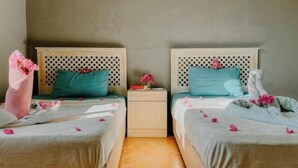 A room with two beds, each with a headboard featuring a polka dot pattern. There are pillows and a small table with a vase of flowers between the beds. - Eel Garden Villas - mountain view beach side apt. (Dahab)