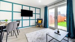 Ein modernes Wohnzimmer mit Essbereich, einem an der Wand befestigten Flachbildfernseher und einer Glastür zum Garten.