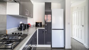 Eine moderne Küche mit Gasherd, schwarzen und weißen Schränken, einem Kühlschrank und einem Wasserkocher.