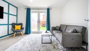 Ein modernes Wohnzimmer mit einem grauen Sofa, einem gelben Sessel, einem weißen Couchtisch und Blick durch eine Glastür ins Freie.