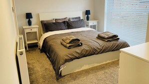 A bedroom with a bed, two bedside tables, a lamp, and a window with blinds.