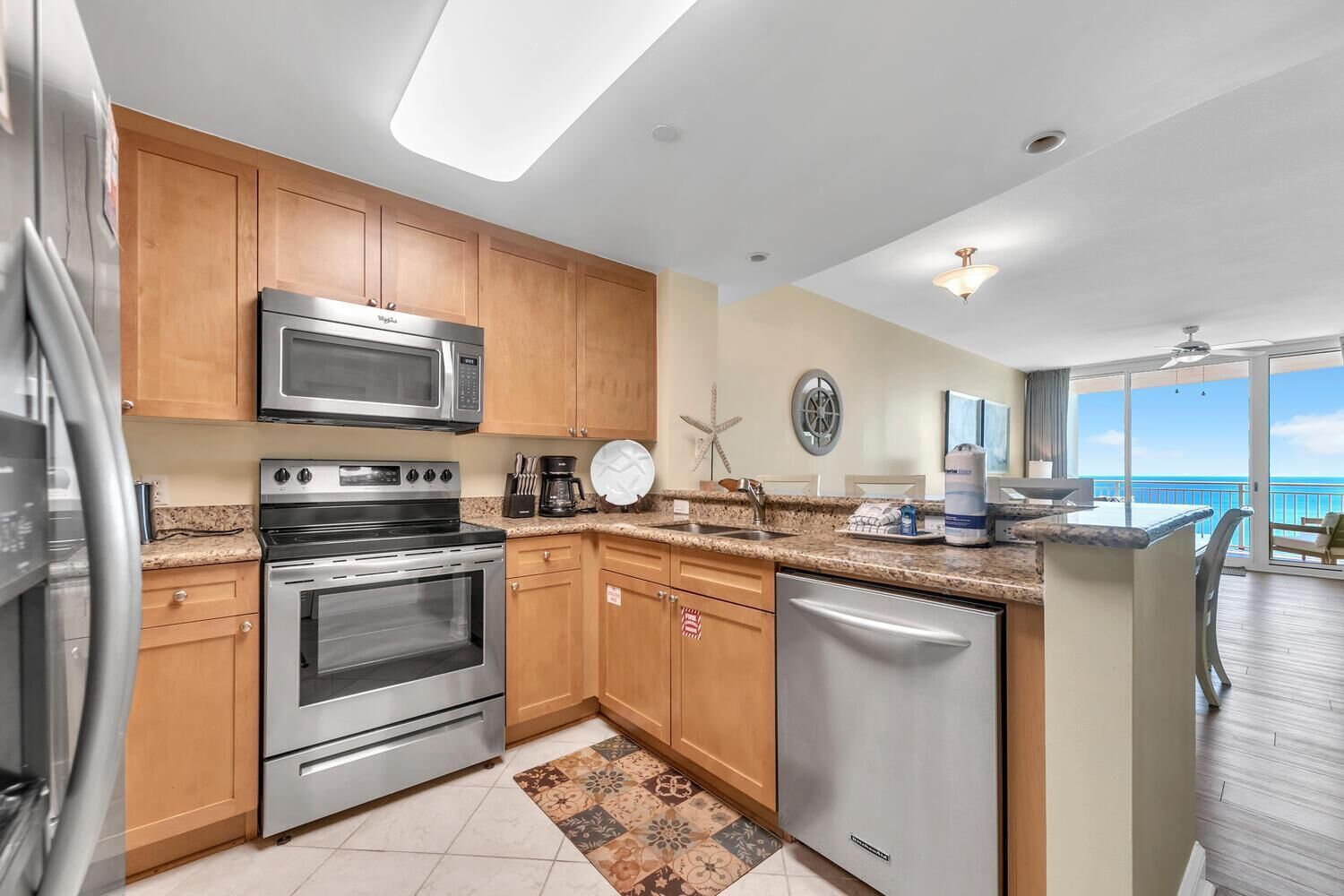 A modern kitchen with stainless steel appliances, wooden cabinets, and a view of the ocean.