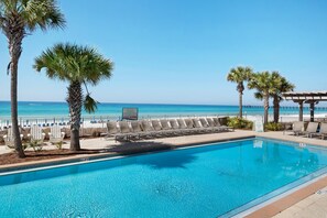 Une piscine avec des chaises longues et des palmiers, donnant sur une plage.