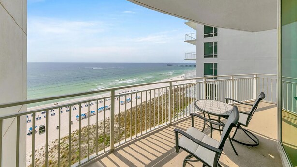Un balcon avec vue sur la plage et l’océan, une table avec des chaises et une rambarde.