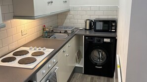 Una cucina compatta con piano cottura, forno a microonde, lavello e lavatrice.