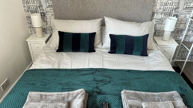 Un letto ben rifatto con una coperta verde acqua, due cuscini e un telecomando su un copripiumino verdeggiante.