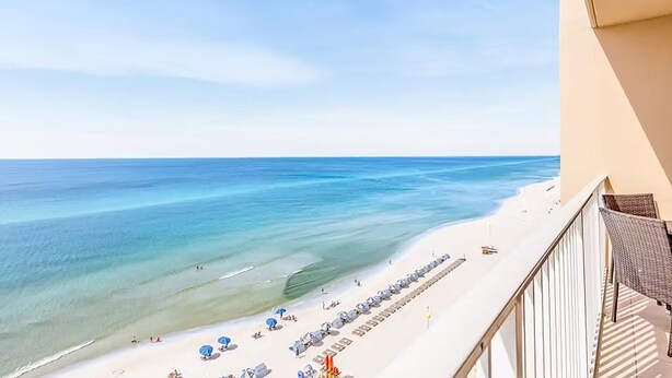 A beach view from a balcony with a row of umbrellas and lounge chairs along the shore. - Tidewater 913 (Panama City Beach)