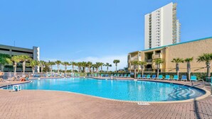 A swimming pool with lounge chairs and palm trees, surrounded by buildings. - Tidewater 913 (Panama City Beach)