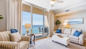 A spacious living room with a balcony, a ceiling fan, and a large window with curtains. - Tidewater 913 (Panama City Beach)