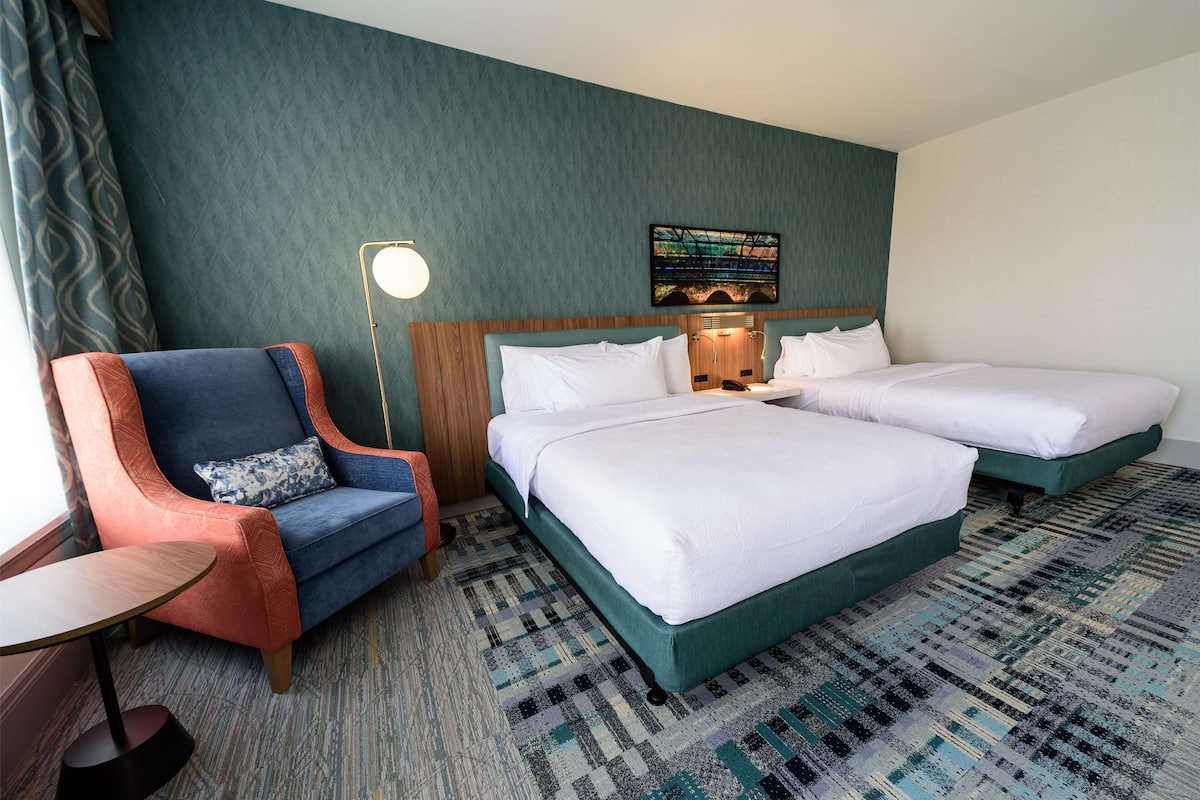 A hotel room with two beds, a sofa, a small table, and a patterned carpet.