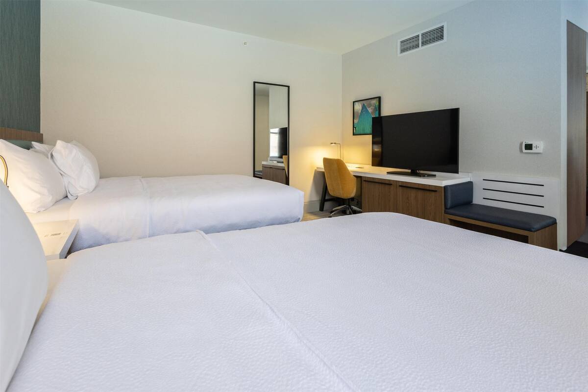 A hotel room with two beds, a desk, a chair, a television, and a mirror.