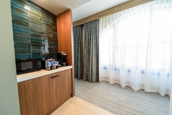 Habitación de hotel compacta con kitchenette, que incluye microondas, cafetera y botellas de agua.