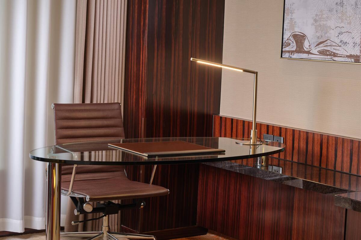 Ein moderner Arbeitsraum mit Glastisch, Ledersessel und Schreibtischlampe.
