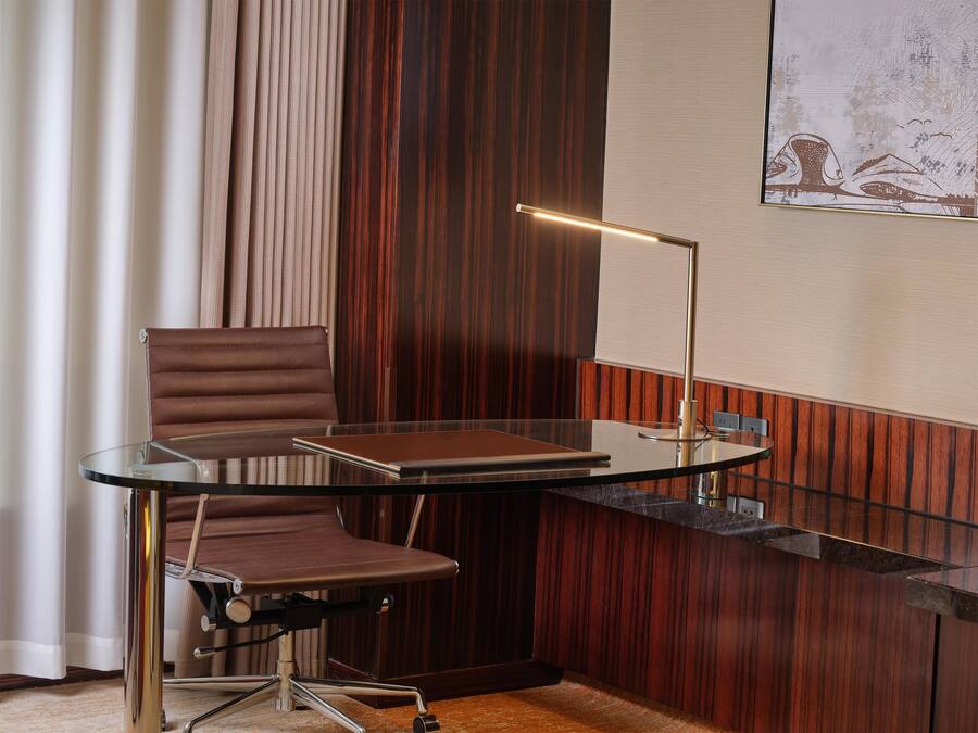 Um espaço de escritório moderno com escrivaninha de vidro, cadeira de couro e luminária de mesa.