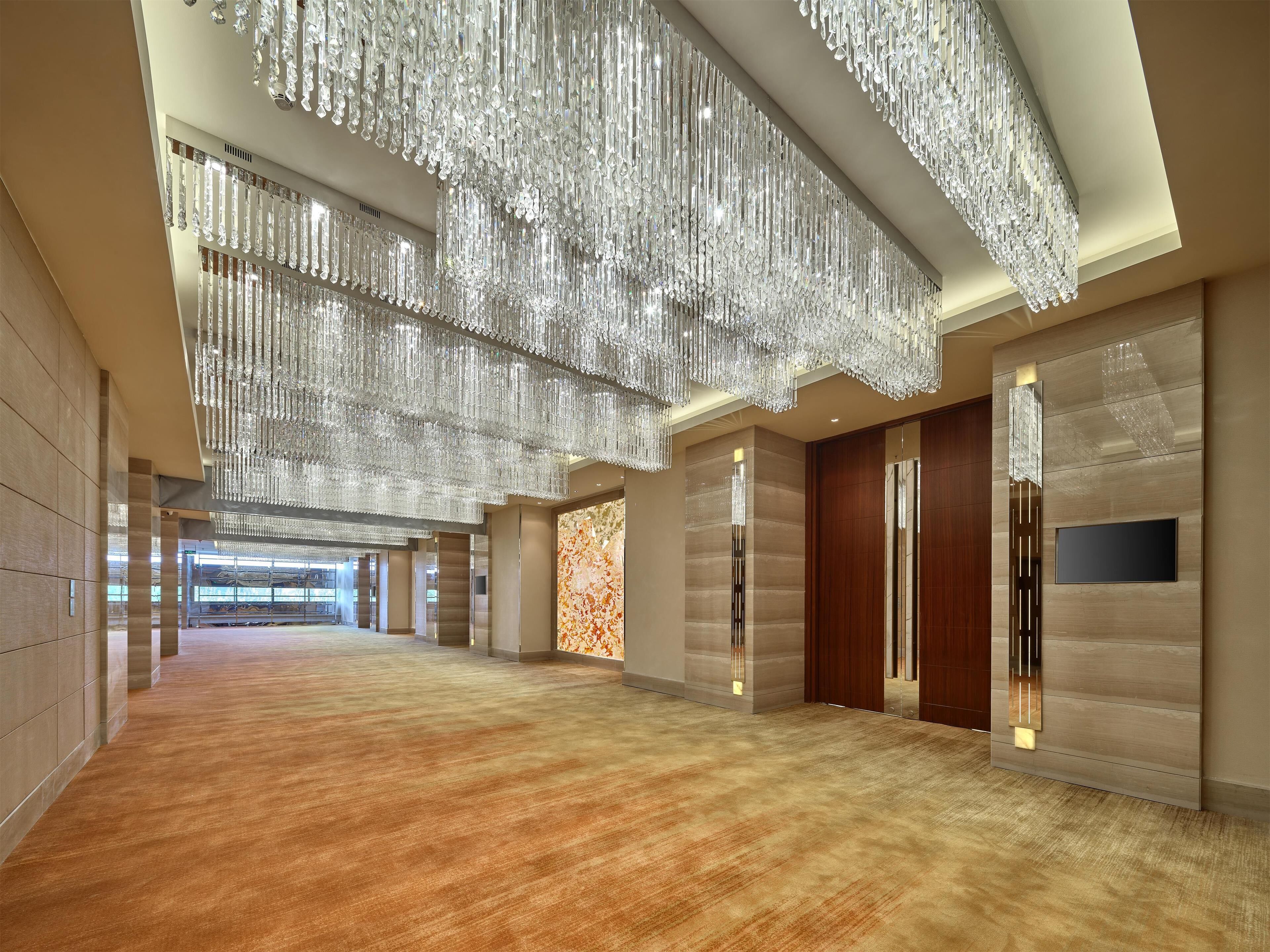 Un hall d’entrée spacieux, doté d’un parquet ciré, de lustres modernes et d’un grand téléviseur fixé au mur.