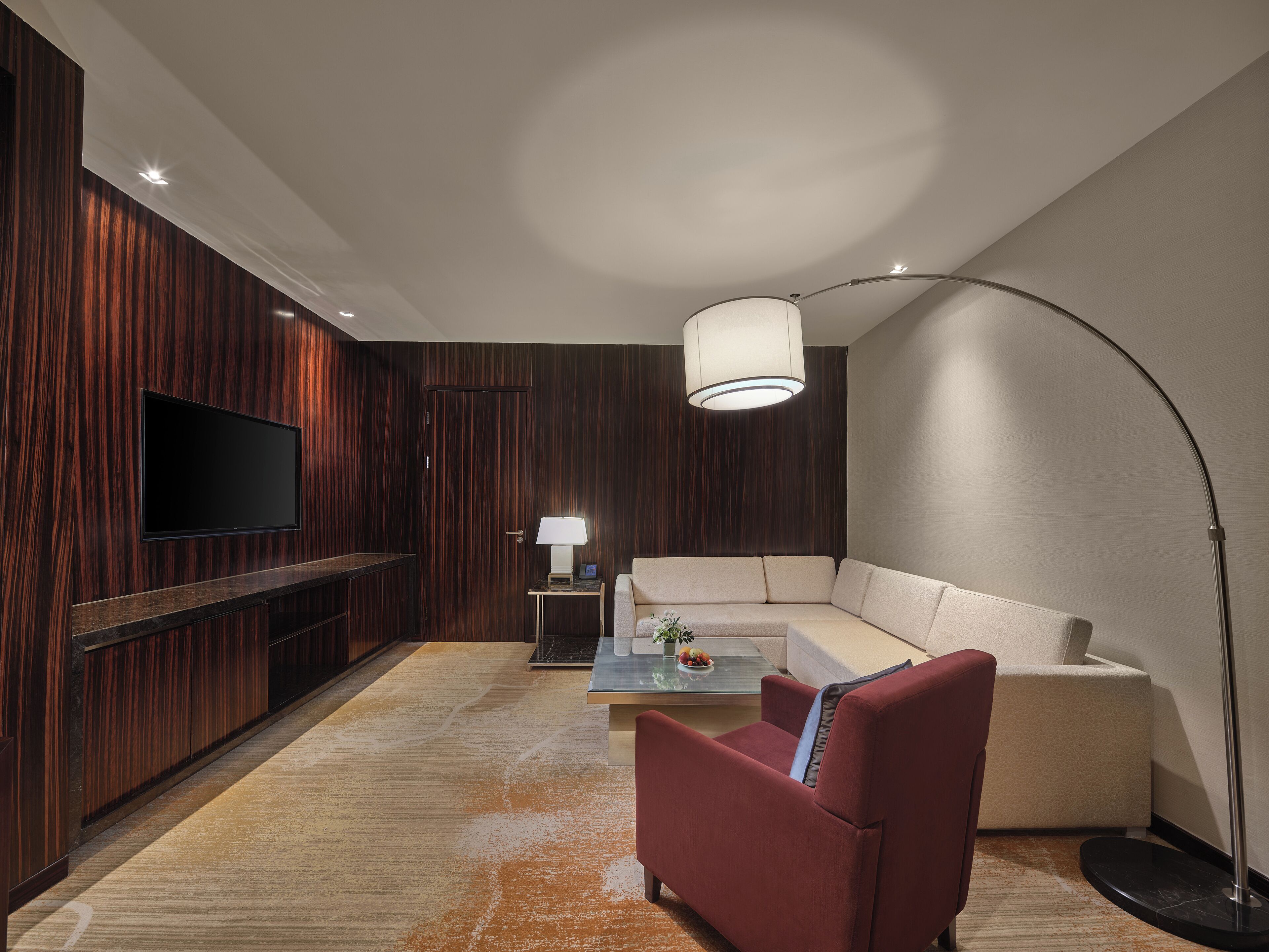 A modern living room with a flat-screen TV, a sofa, a red armchair, a coffee table, and a floor lamp.