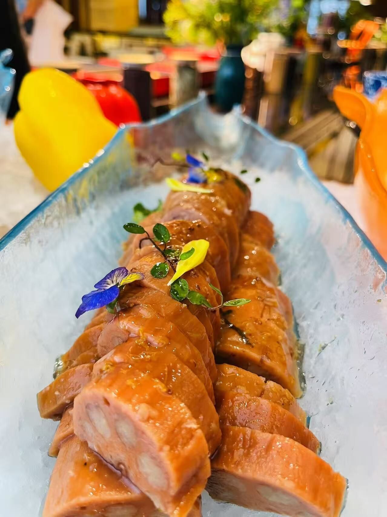 A glass dish with sliced salmon on ice, garnished with herbs and edible flowers.