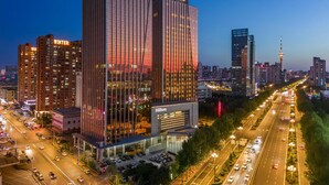 A high-rise hotel with a prominent 'Hilton' sign, surrounded by a busy urban street and other high-rise buildings. - Hilton Harbin Exhibition Center (Harbin)