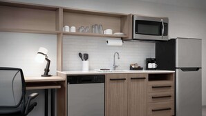 Una cocina moderna equipada con lavavajillas, microondas y refrigerador. Cuenta con una encimera de madera, un lavamanos y una silla.