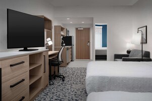 Una habitación de hotel con una cama, un escritorio con ordenador, televisión y una silla.
