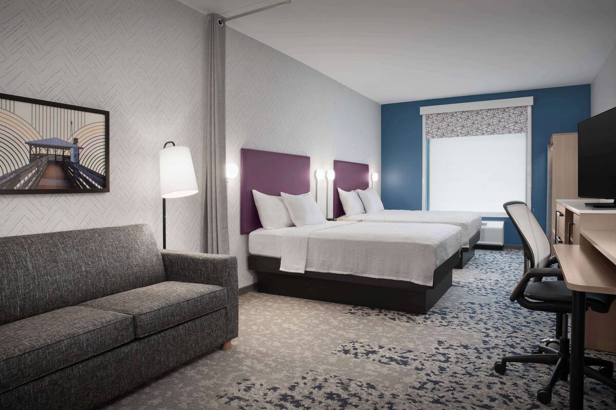 A hotel room with a bed, a sofa, a desk, and a TV.