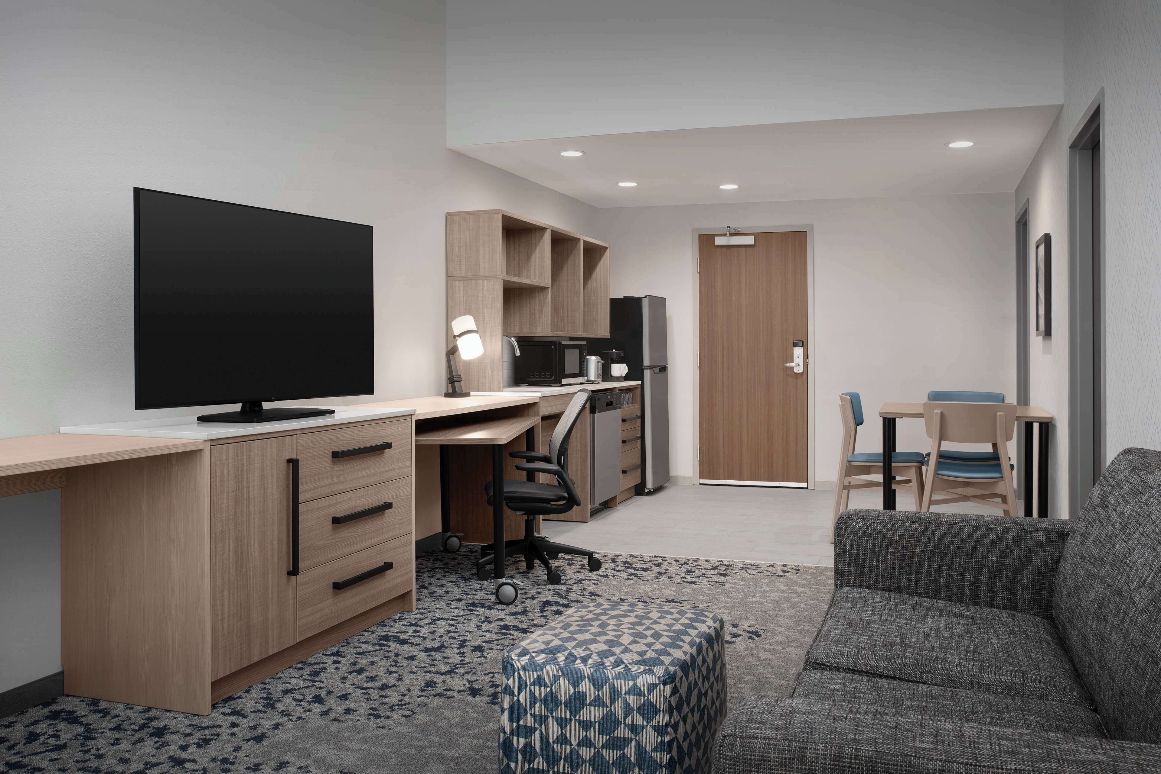 A modern, compact living space with a flat-screen TV, a kitchenette, a sofa, and a dining area.