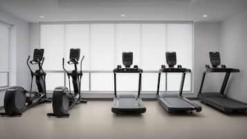 Ein Fitnessraum mit fünf Trainingsgeräten, darunter Laufbänder und ein Crosstrainer, ausgestattet mit großen Fenstern und einer weißen Decke.