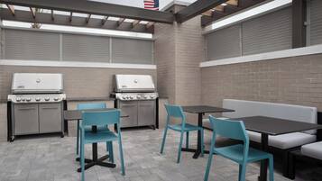 Une terrasse extérieure équipée de deux barbecues, de quatre chaises et d’une table.
