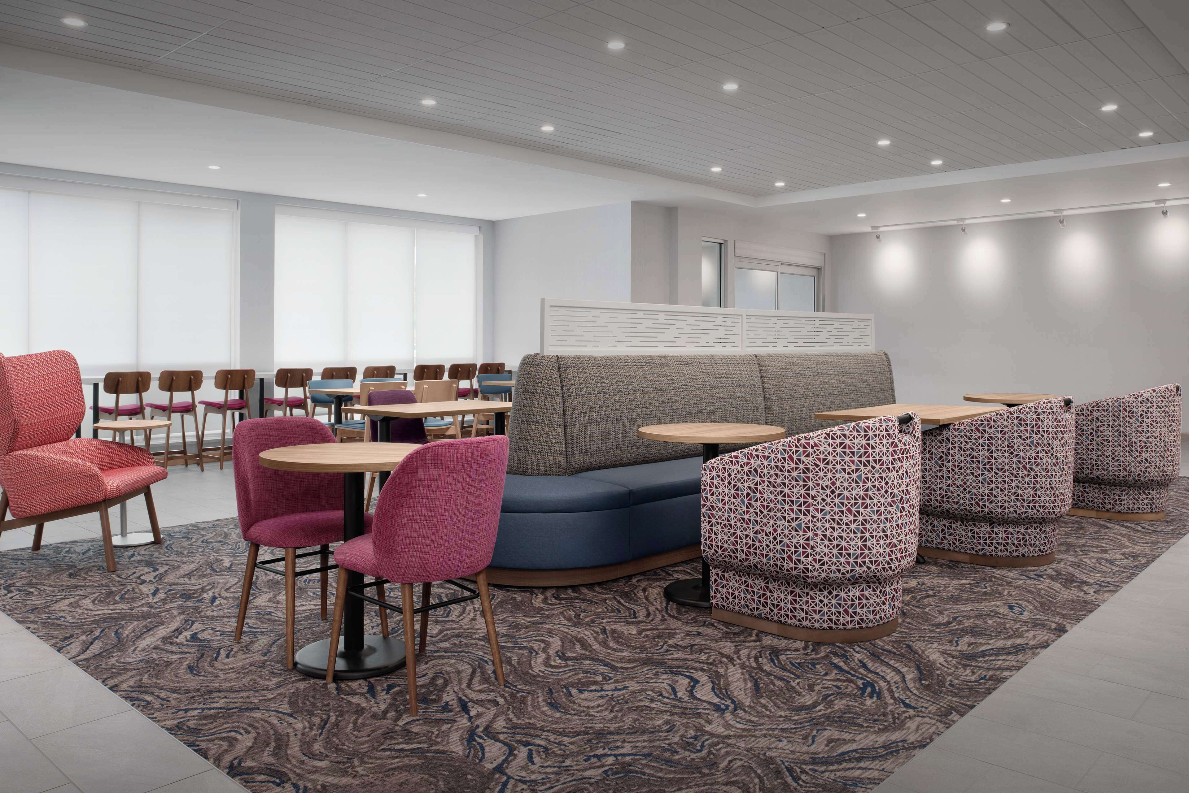 A modern lounge area with seating arrangements, including a blue sofa, pink chairs, and patterned stools.