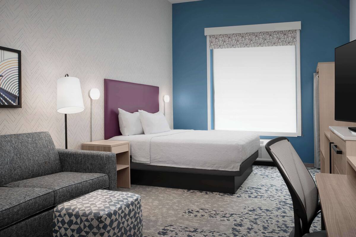 A hotel room with a bed, a sofa, a desk, and a TV.
