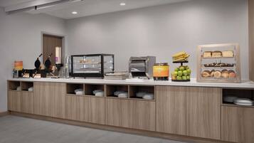 A modern breakfast bar with a variety of food options including waffles, oatmeal, bananas, apples, and pastries.