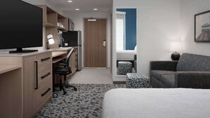 Una habitación de hotel moderna con una cama grande, un escritorio con computadora y silla, un sofá y una mesita.