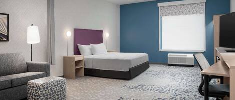 Ett hotellrum med en säng, ett skrivbord, en stol, en soffa och en mönstrad pall.
