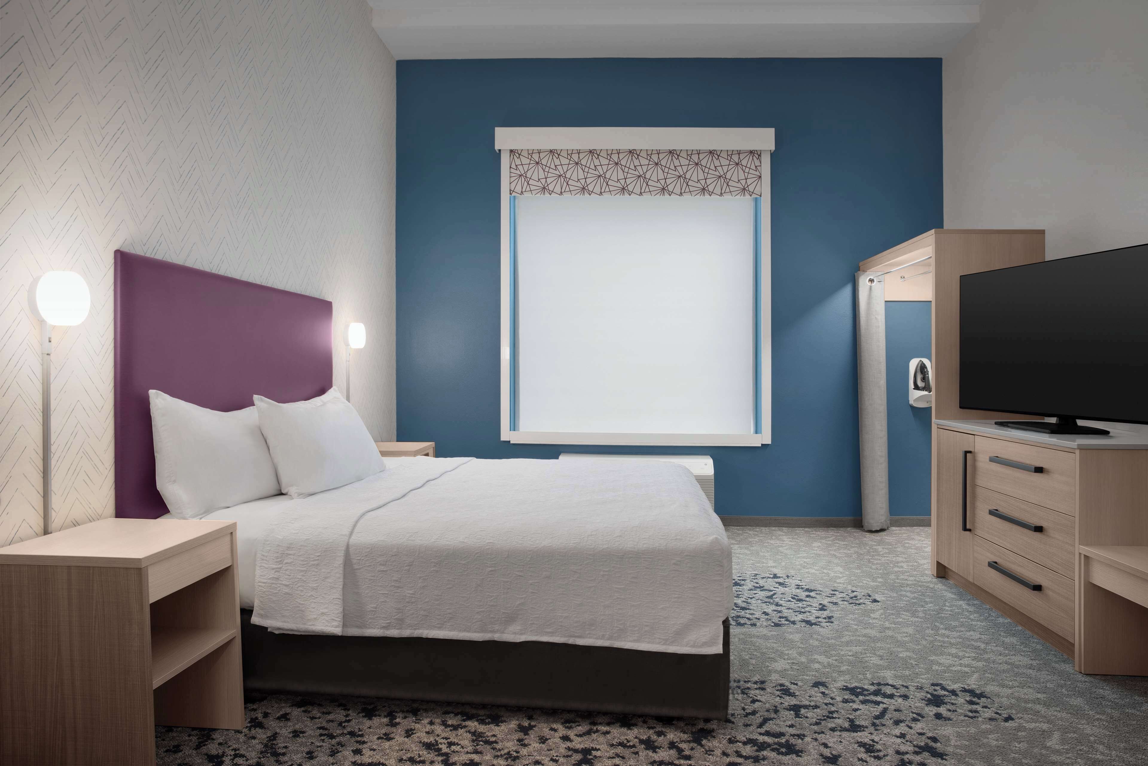 A modern bedroom with a bed, bedside tables, a TV, and a window with a patterned curtain.