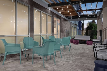 An outdoor patio with teal chairs and a fire pit, large windows, and a covered area with string lights.