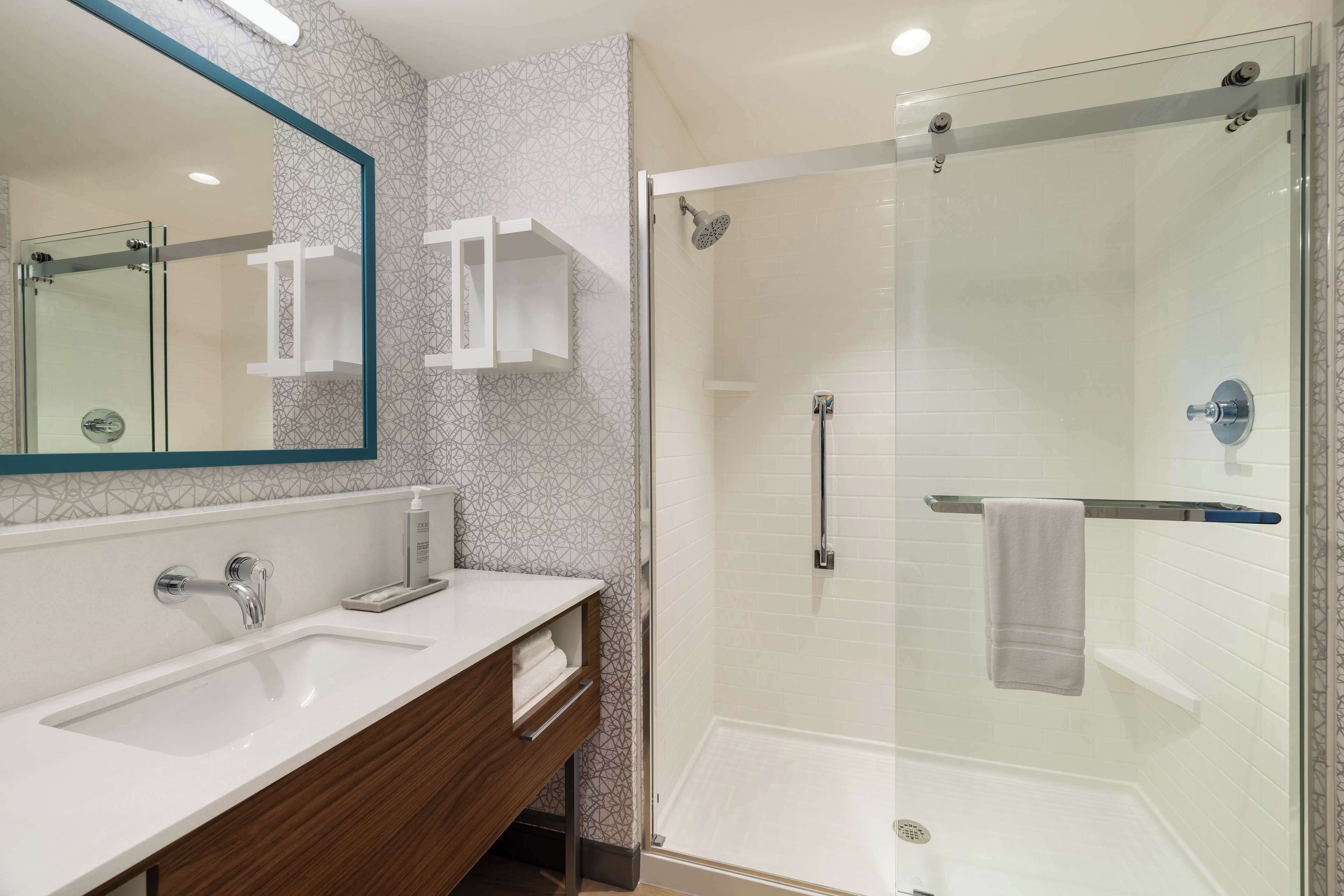A modern bathroom with a glass-enclosed shower, a large mirror, and a white sink.