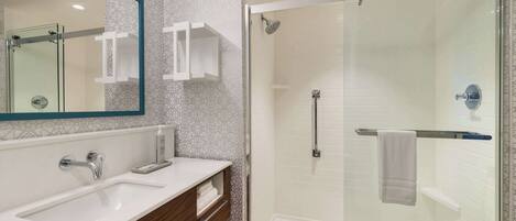 A modern bathroom with a glass-enclosed shower, a large mirror, and a white sink.