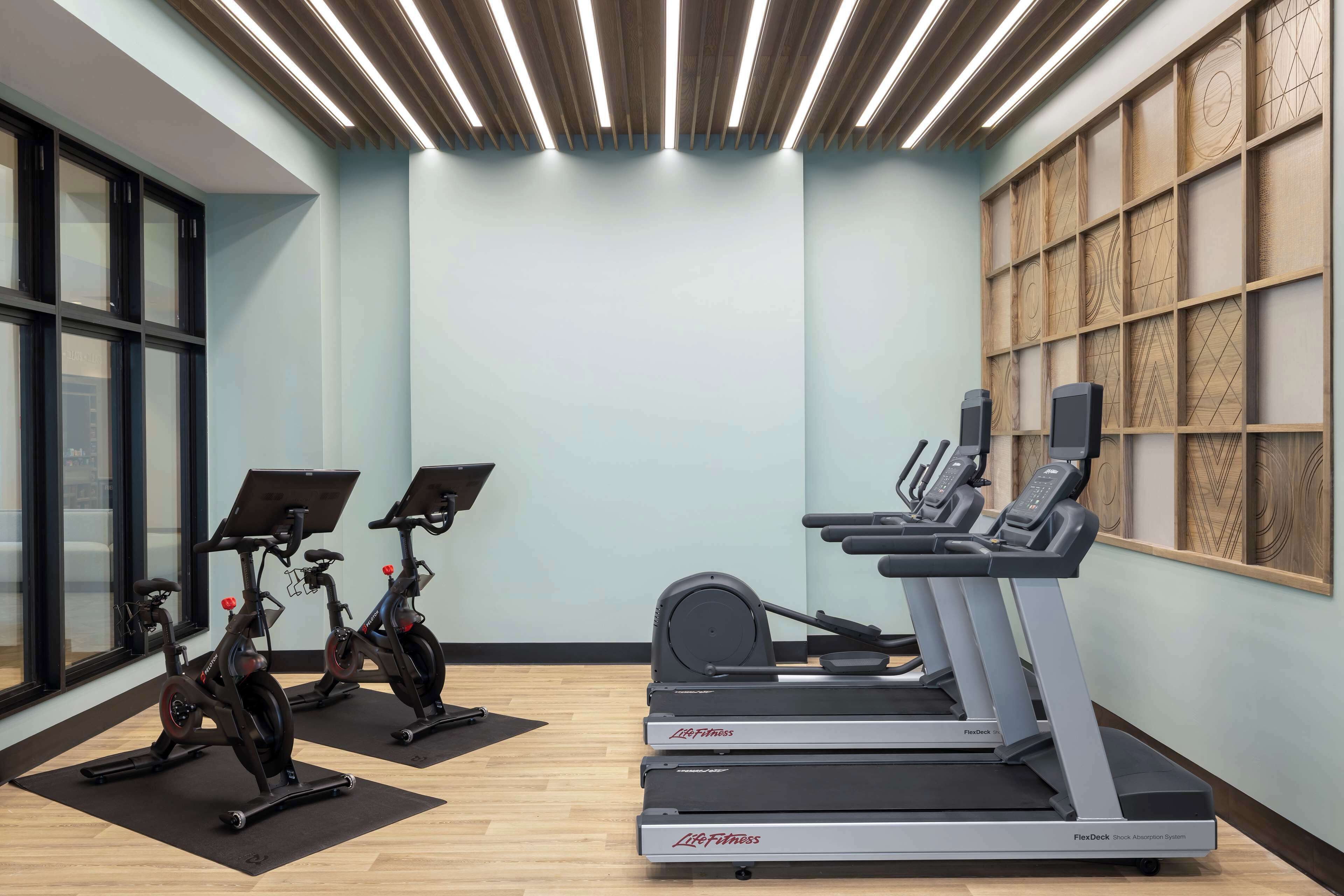 A gym with cardio equipment, including stationary bikes and treadmills, and large windows on one side.