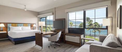 Habitación de hotel con cama, escritorio, silla y un ventanal con vistas al mar.