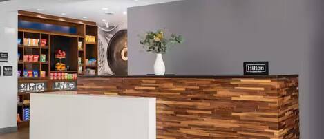 A reception desk with a wood grain design, a potted plant, and a sign indicating it's a Hilton hotel.