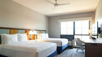 A hotel room with two beds, a desk, a chair, and a large window.