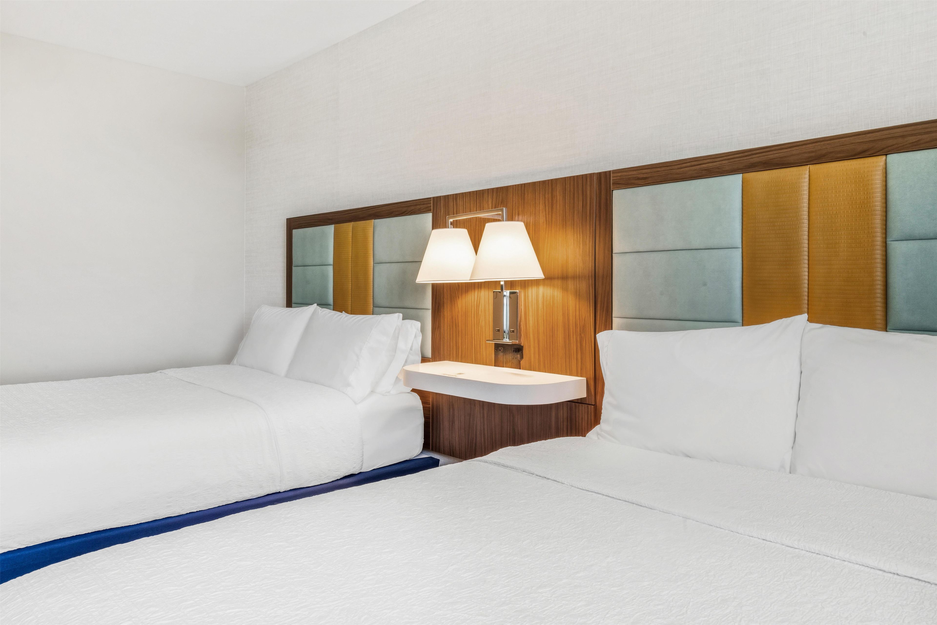 A hotel room with two beds, a bedside table, a lamp, and a wooden headboard.
