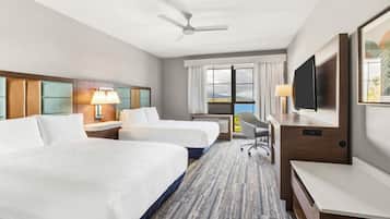 A hotel room with two beds, a desk, a TV, and a view of the outdoors.