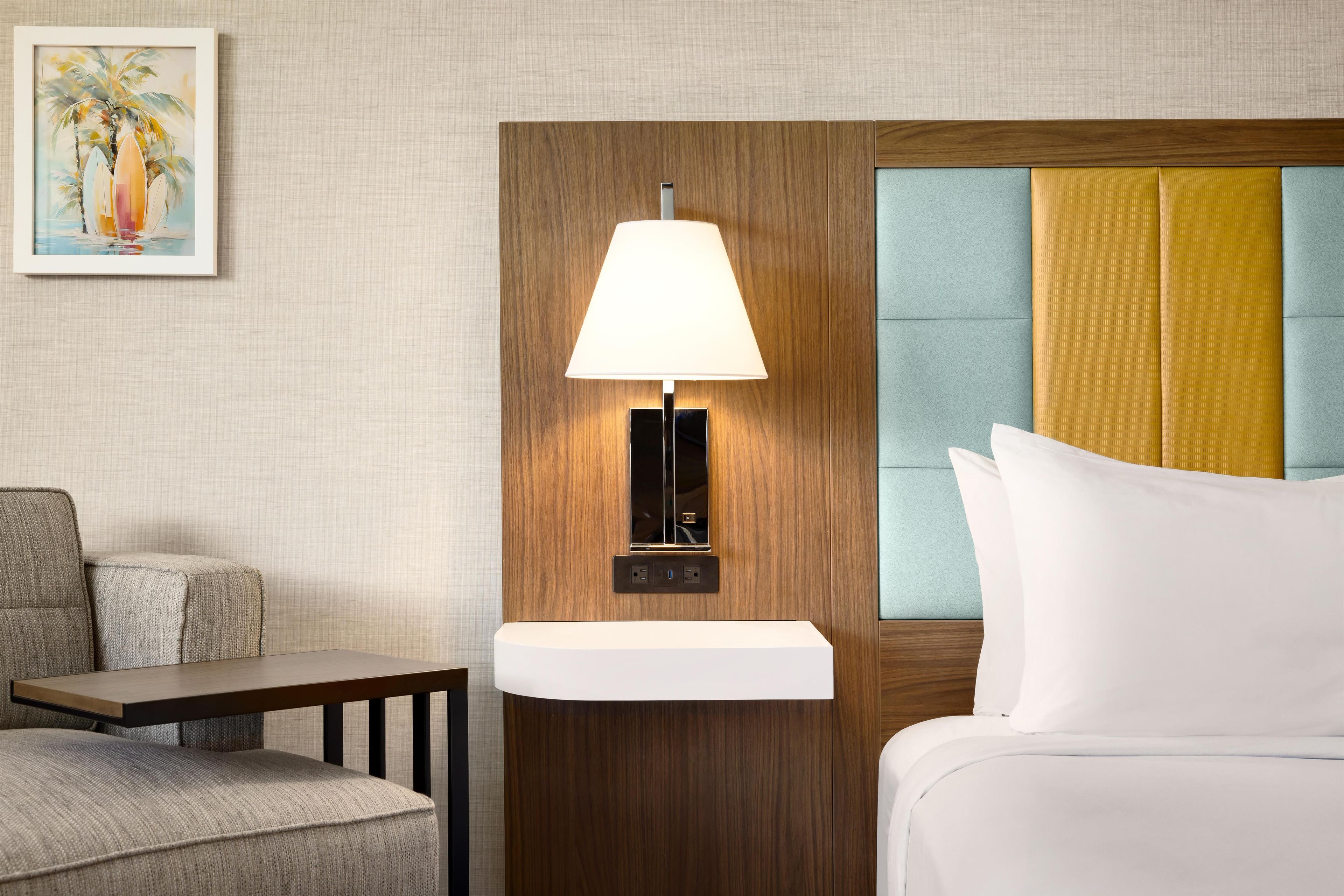 Ein Hotelzimmer mit einem Holzkopfteil, einem Nachttisch, einer Lampe und einem Bett mit weißer Bettwäsche.